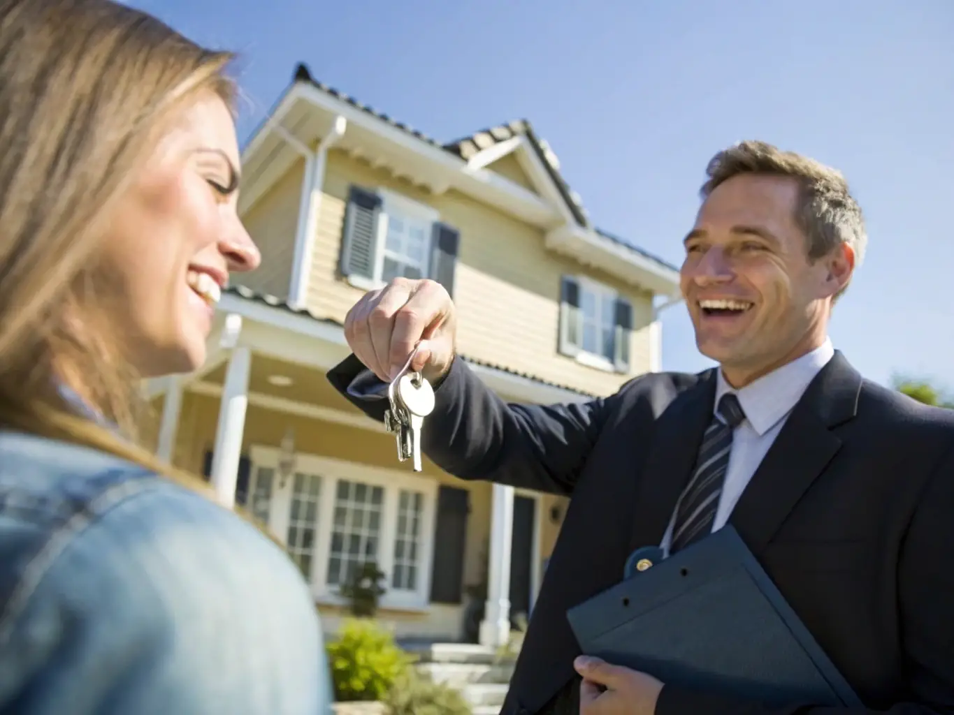 A real estate agent is handing over keys to a smiling client in front of a modern apartment building, symbolizing property ownership and satisfaction.